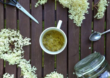 Mürver çiçeği ahşap masada, çay fincanı, taze bitkisel çiçek, kurutulmuş bir bardak, çay kaşığı, makas.