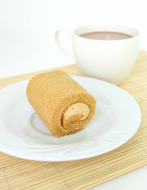 çikolatalı pasta rulo beyaz tabak ve bardak kahve ahşap mat.