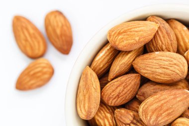 Beyaz arka plan üzerinde beyaz kase üst görünümünde badem.