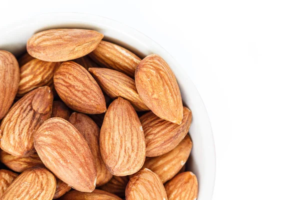 Beyaz arka plan üzerinde beyaz kase üst görünümünde badem.