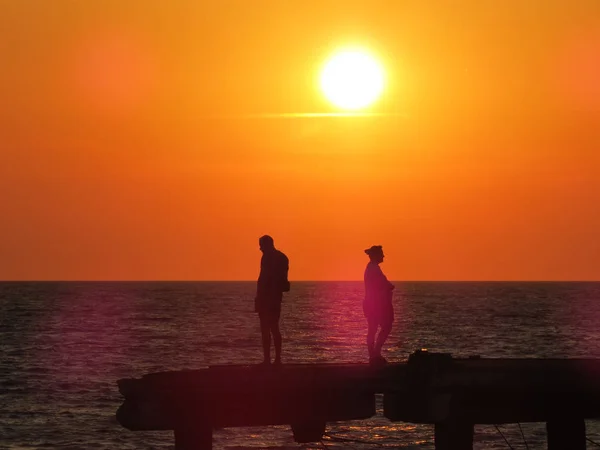 Two silhouettes of people at sunset against the sun and the sea