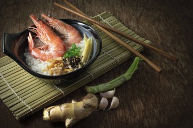 Pirinç Bulamaç karides ve zencefil, yeşil soğan dilimi ve derin kızarmış sarımsak ve kara biber siyah kase karışık. baharat önünde ve ahşap elek ve ahşap arka plan üzerinde sağ tarafta ahşap çubuk koydu