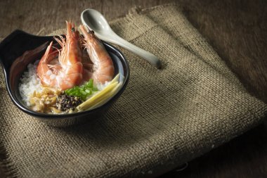 Pirinç Bulamaç karides ve zencefil, yeşil soğan dilimi ve derin kızarmış sarımsak ve kara biber siyah kase karışık. Seramik kaşık geri koymak yan ahşap arka plan ve çuval