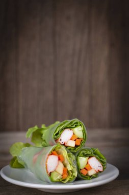 Ahşap bir masa yerleştirilmiş beyaz tabakta salata rulo.