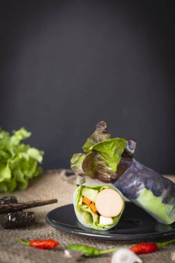 Salata bir çuval biber ile yerleştirilen siyah plaka üzerinde rulo ve sarımsak önünde yer yanında yer chopsticks ve marul arka yüzünde yer