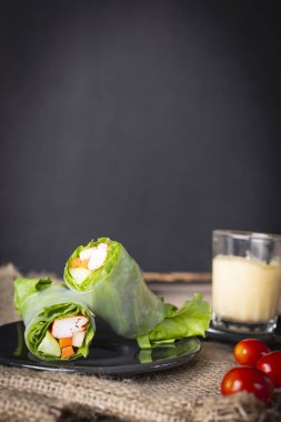 Salata domates ve salata sosu yanında yerleştirilen bir çuval yerleştirilen siyah plaka üzerinde rulo.