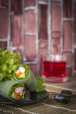 Salata yanında yer chopsticks ve kırmızı su cam arka yerleştirilen bir ahşap elek yerleştirilen siyah plaka üzerinde rulo.