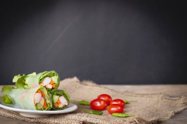 Salata domates ve biber yanında yerleştirilen bir çuval yerleştirilmiş beyaz plaka üzerinde rulo.