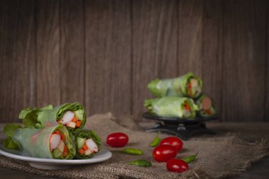 Salata domates ve biber yanında yerleştirilen bir çuval yerleştirilmiş beyaz plaka üzerinde rulo ve salata arka yerleştirilen siyah plaka üzerinde rulo.