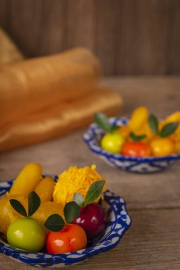 Beyaz ve mavi çizgili bir tabakta Tay tatlılar vardır ahşap masa üzerinde yerleştirilen benzer nesne ve bir altın bez koyun arka. 