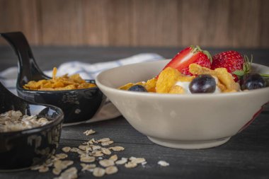 Kumaş, yulaf ezmesi, Mısır gevreği ve çevresinde yer bardakta süt çilek ve üzüm tepesi ile mavi ve beyaz tahta masada beyaz kase yoğurt karışımı yulaf ezmesi, çizgili.