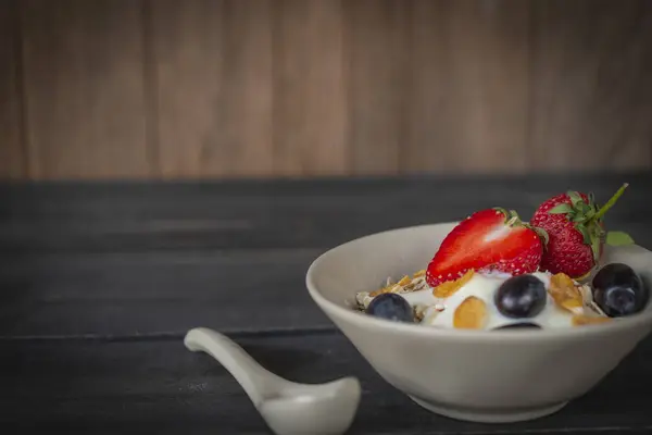 酸奶混合燕麦片 草莓和葡萄在白色碗在木桌上与勺子放在旁边 — 图库照片