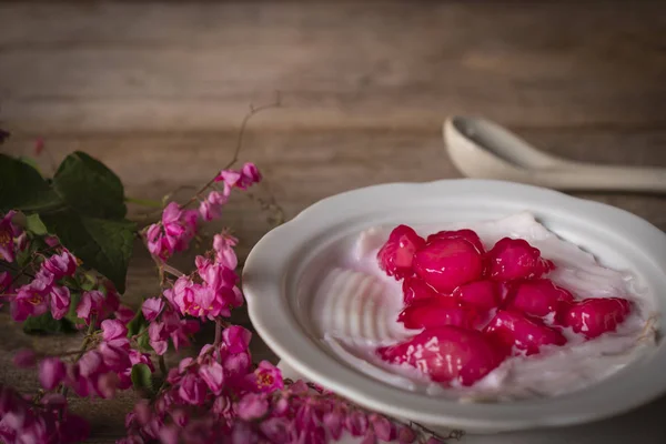 Thapthim krop, pseudo-Granatapfelkerne in Kokosnuss und Sirup in der weißen Schüssel auf dem Holztisch liegen Blumen und Löffel herum. — Stockfoto