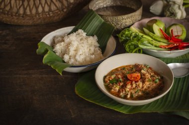 Tay Kuzey Tarzı Domuz eti ve Domates Chili Relish, ahşap masada beyaz kase içinde nam prik ong taze sebze, pişmiş pirinç, su kase ve çiçek yan yemekler arka tarafı yerleştirilir.