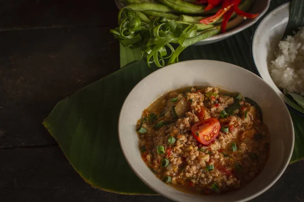 Thai Northern style wieprzowina i pomidor chili Relish, nam Prik Ong w białej misce na drewnianym stole są boczne dania ze świeżych warzyw i gotowane ryż umieszczony z powrotem strony. — Zdjęcie stockowe