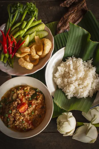 Thai Northern Style Pork and Tomato Chili Relish, nam prik ong in white bowl on wood table there are side dishes of fresh vegetables, cooked rice and flower placed around. — Stock Photo, Image