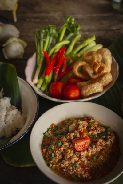 Thai Northern style wieprzowina i pomidor chili Relish, nam Prik Ong w białej misce na drewnianym stole są boczne dania ze świeżych warzyw, gotowane ryż i kwiat umieszczony z powrotem strony. — Zdjęcie stockowe