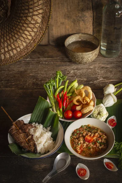 Thai Northern Style Pork and Tomato Chili Relish, nam prik ong in ciotola bianca sul tavolo di legno ci sono contorni di verdure fresche, riso cotto, ciotola d'acqua e fiori disposti intorno. . — Foto Stock