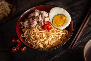 Odun masada siyah kase üzerinde domuz eti, yumurta ve sebze ile Anlık erişte var biber, çubuk, siyah plaka anında erişte ve içme cam etrafında yerleştirilir.