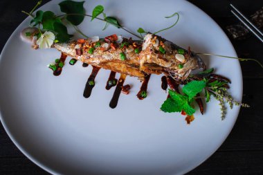 Beyaz tabak ve dekorasyon ile beyaz tabak ve dekorasyon ile Kızarmış Saba balık ahşap masa üzerine kaplanmış, yanında yerleştirilmiş çubuk var.