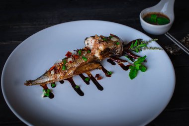Beyaz tabak ve dekorasyon ile beyaz tabak ve dekorasyon ile Kızarmış Saba balık ahşap masaya kaplanmış, kaşık seramik ve çubuk arka tarafında yerleştirilen sos vardır.