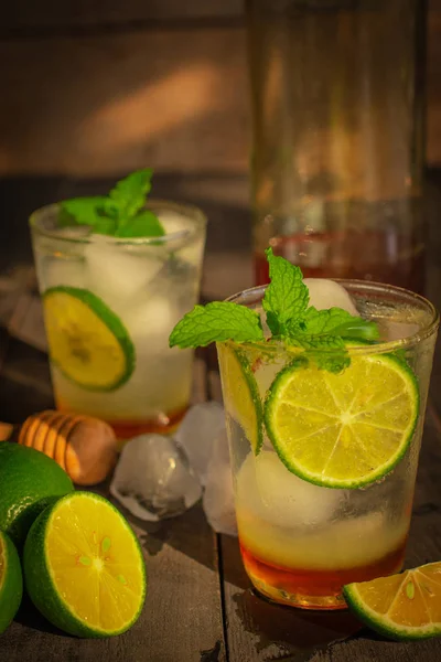 Fresh Ice Honey Lemon soda drink on the wood table there are lemon slice, ice, honey in glass bottle and wooden honey dipper placed around.