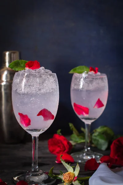 Sparkling cold water detox with rose and ice on the wood table there are rose, same object and cocktail shaker placed around.