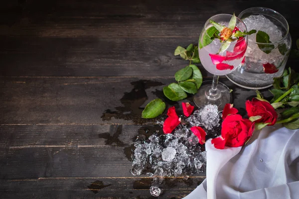 Sparkling cold water detox with rose and ice on the wood table there are rose, diferance glass and ice placed around.