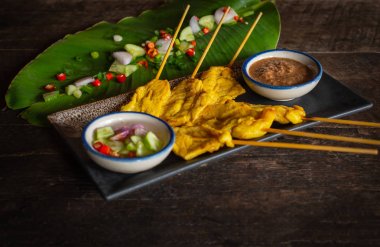 Ahşap masaya yerleştirilen siyah plaka üzerinde tay baharat ve fıstık sosu ile domuz satay.