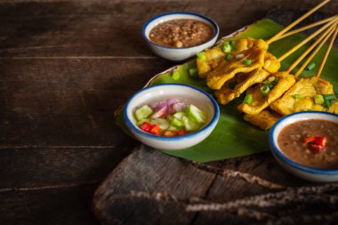 Ahşap masaya yerleştirilen muz yaprağı üzerinde tay baharat ve fıstık sosu ile domuz satay.