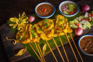 Ahşap masaya yerleştirilen muz yaprağı üzerinde tay baharat ve fıstık sosu ile domuz satay.