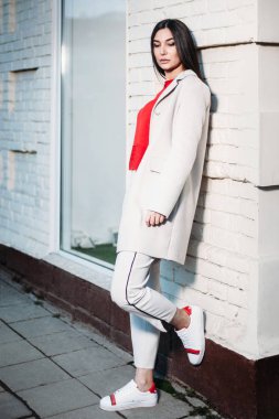 Beyaz tuğla duvara yakın açık havada kentsel arka planda duran genç güzel esmer kadın portresi