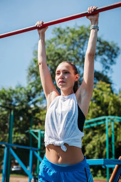 ストリート トレーニングの女の子 彼女のプルアップ自分まで公園内のグラウンドにバーの上 — ストック写真