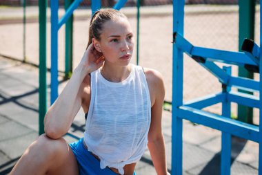 Sporcu genç sarışın kadın spor sahasında antrenmanlardan sonra dinleniyor.