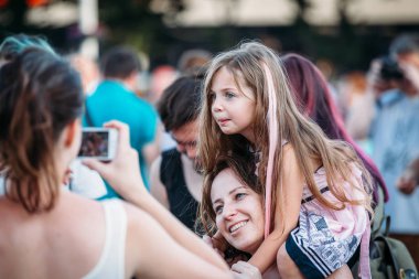 Yessentuki, Stavropol bölge / Rusya - 12 Ağustos 2017: güzel güzel kız çocuk sarışın anne omuzlarında oturan pembe saçlı, onlar fotoğraflandı ve izlerken konser açık havada
