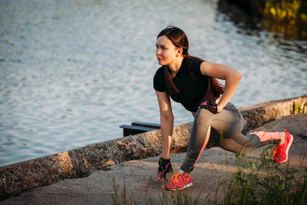 Молодая спортсменка делает упражнения в парке возле озера — стоковое фото