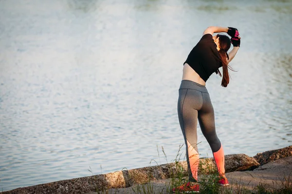 Młoda kobieta lekkoatletycznego robi ćwiczenia zgięcia side w parku w pobliżu jeziora. — Zdjęcie stockowe