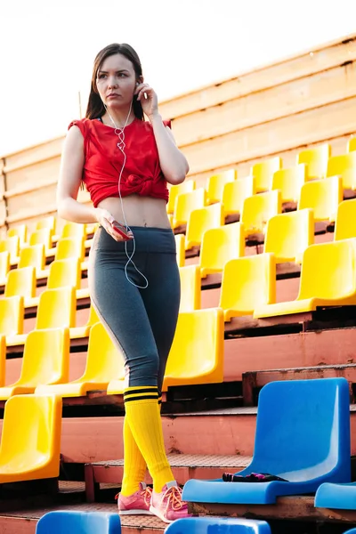 Молодая спортсменка в спортивной одежде на трибунах стадиона слушает — стоковое фото