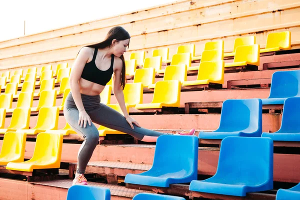 Молодая женщина делает упражнения на растяжку на трибуне стадиона — стоковое фото