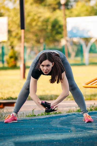 Młoda kobieta lekkoatletycznego ćwiczeń wychyla się do przodu w parku się — Zdjęcie stockowe