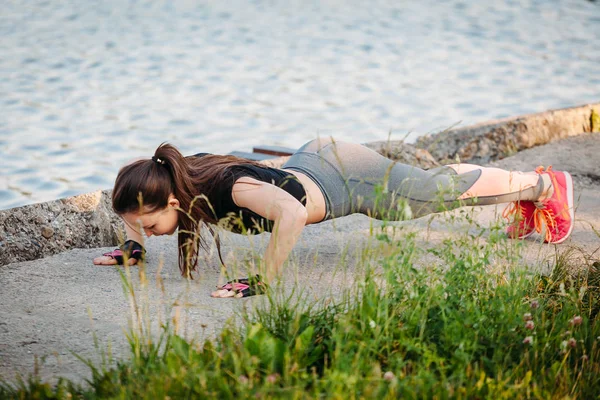 Jovem mulher fazendo Push-Upsin no parque contra lago — Fotografia de Stock