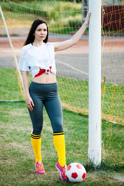 Ung flicka poserar med fotboll på fotbollsmål — Stockfoto