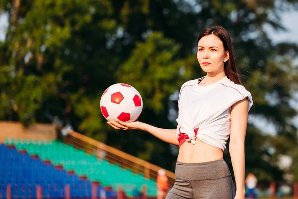 Žena s fotbalovým míčem v rukou na fotbalové hřiště na backgro — Stock fotografie