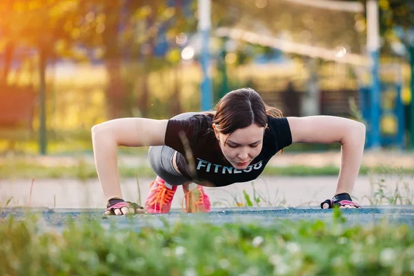 Belle brune mince faisant quelques push-ups à l'extérieur dans le parc. Ajustement — Photo