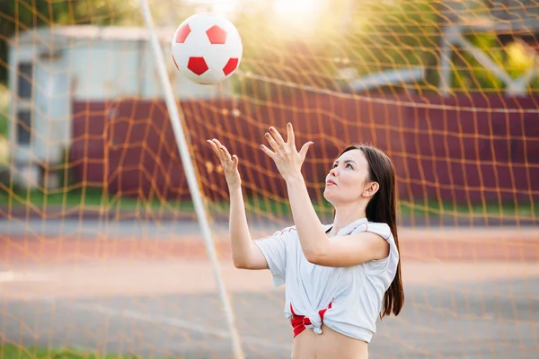 女性は、foo のグリッドの背景にスタジアムでサッカー ボールを投げる — ストック写真