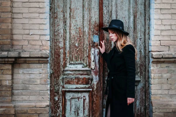 Blonde girl with long hair, in black coat in hat, stands on the — Stock Photo, Image