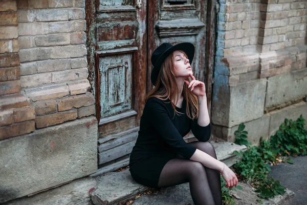 Blonde dreaming girl with long hair, in black dress in hat, is s — Stock Photo, Image