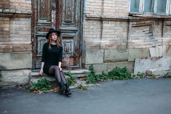 Blonde pensive girl with long hair, in black dress in hat, is si — Stock Photo, Image