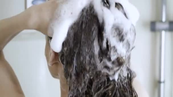 A girl is washing her hair. White foam from the shampoo on long hair brunettes — Stock Video