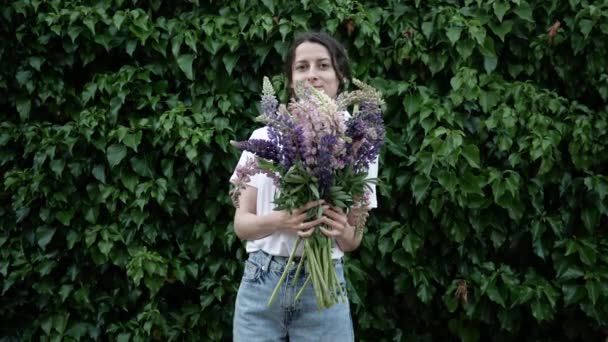 Vacker ung kvinnlig florist håller bukett på väggen bakgrund och erbjuder sig att köpa den för dig — Stockvideo